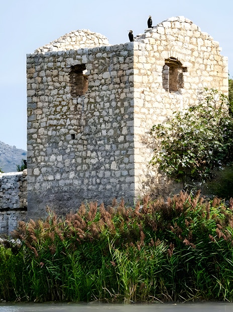 Grmožur Fortress ruins by a lake with mountain backdrop.