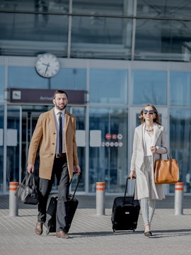 Travelers with luggage outside Amsterdam airport terminal.