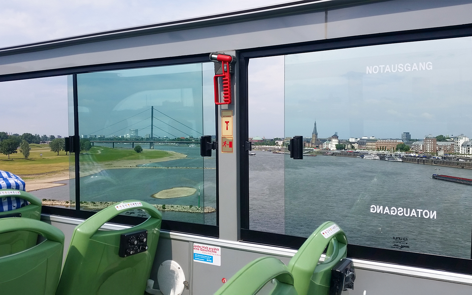 Open-top bus view of Rhine River and Dusseldorf skyline during hop-on hop-off city tour.