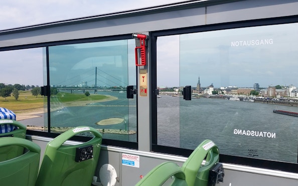 Open-top bus view of Rhine River and Dusseldorf skyline during hop-on hop-off city tour.