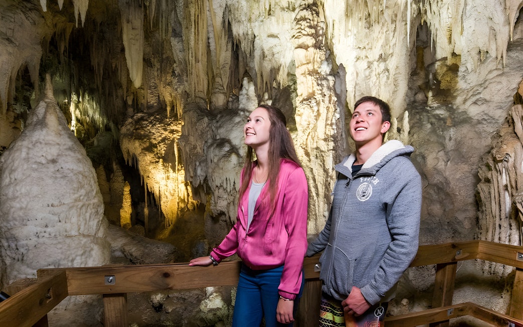 Visitors exploring Waitomo Glowworm Caves in Auckland, viewing stalactites and stalagmites.