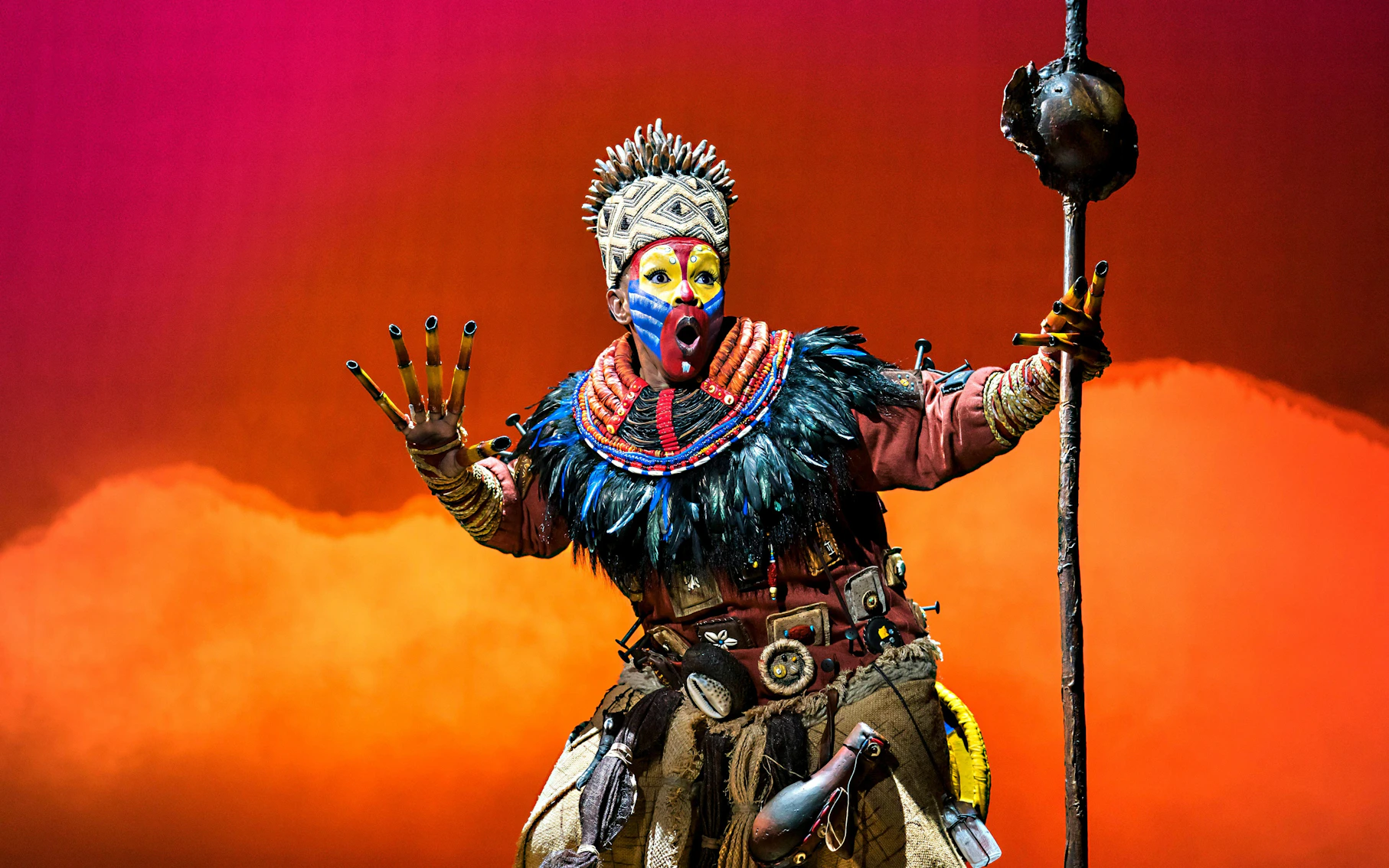 Performer in vibrant costume from The Lion King musical on stage.