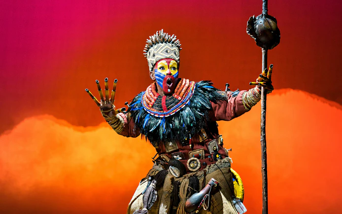 Performer in vibrant costume from The Lion King musical on stage.