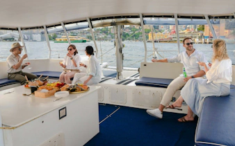 Tourists enjoying food and drinks on a Sydney Harbour cruise at sunset.
