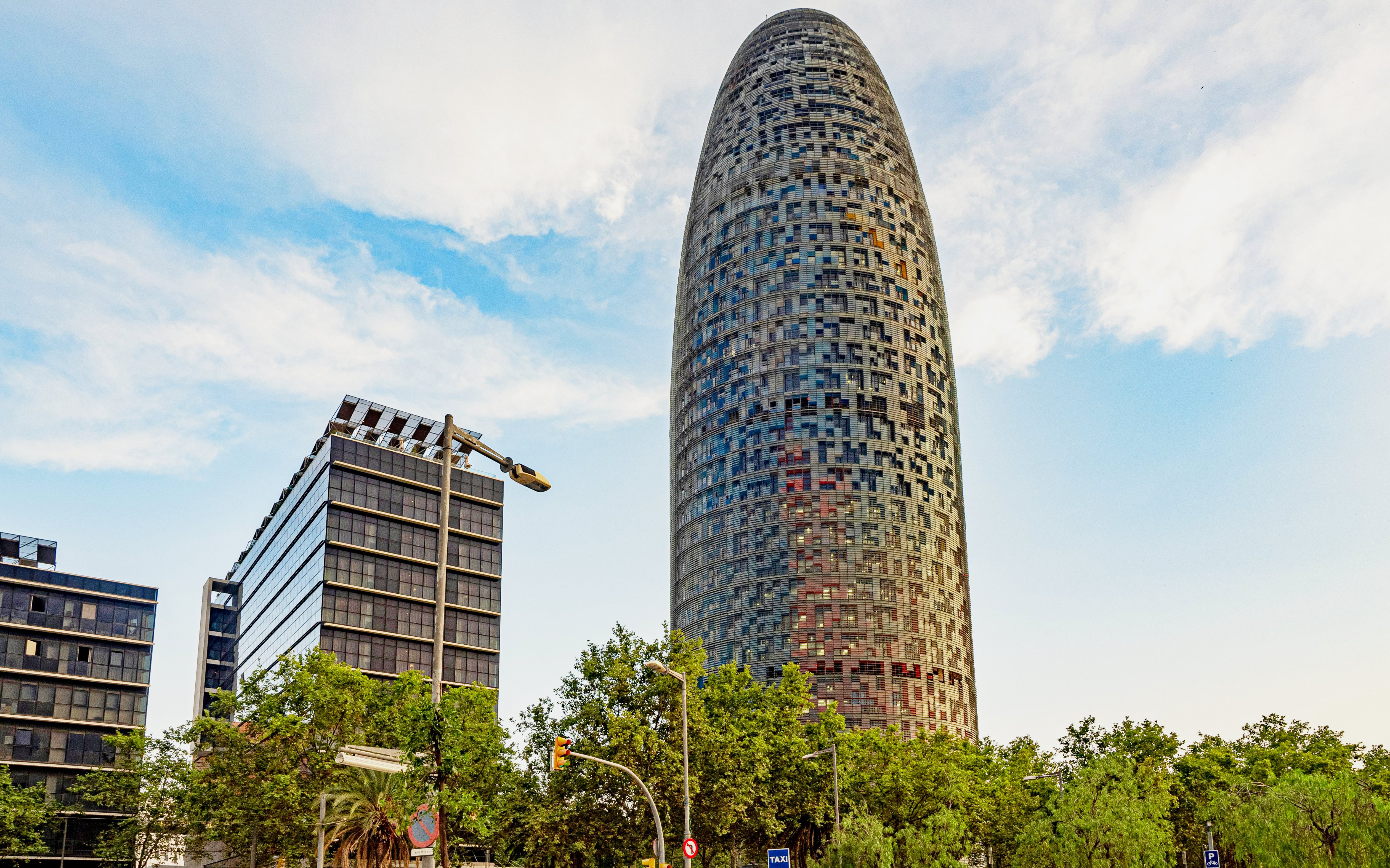 Torre Glòries in Barcelona with surrounding modern buildings and trees.