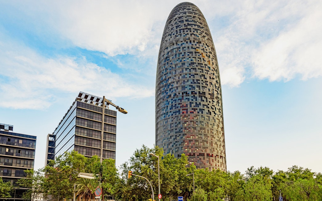 Torre Glòries in Barcelona with surrounding modern buildings and trees.