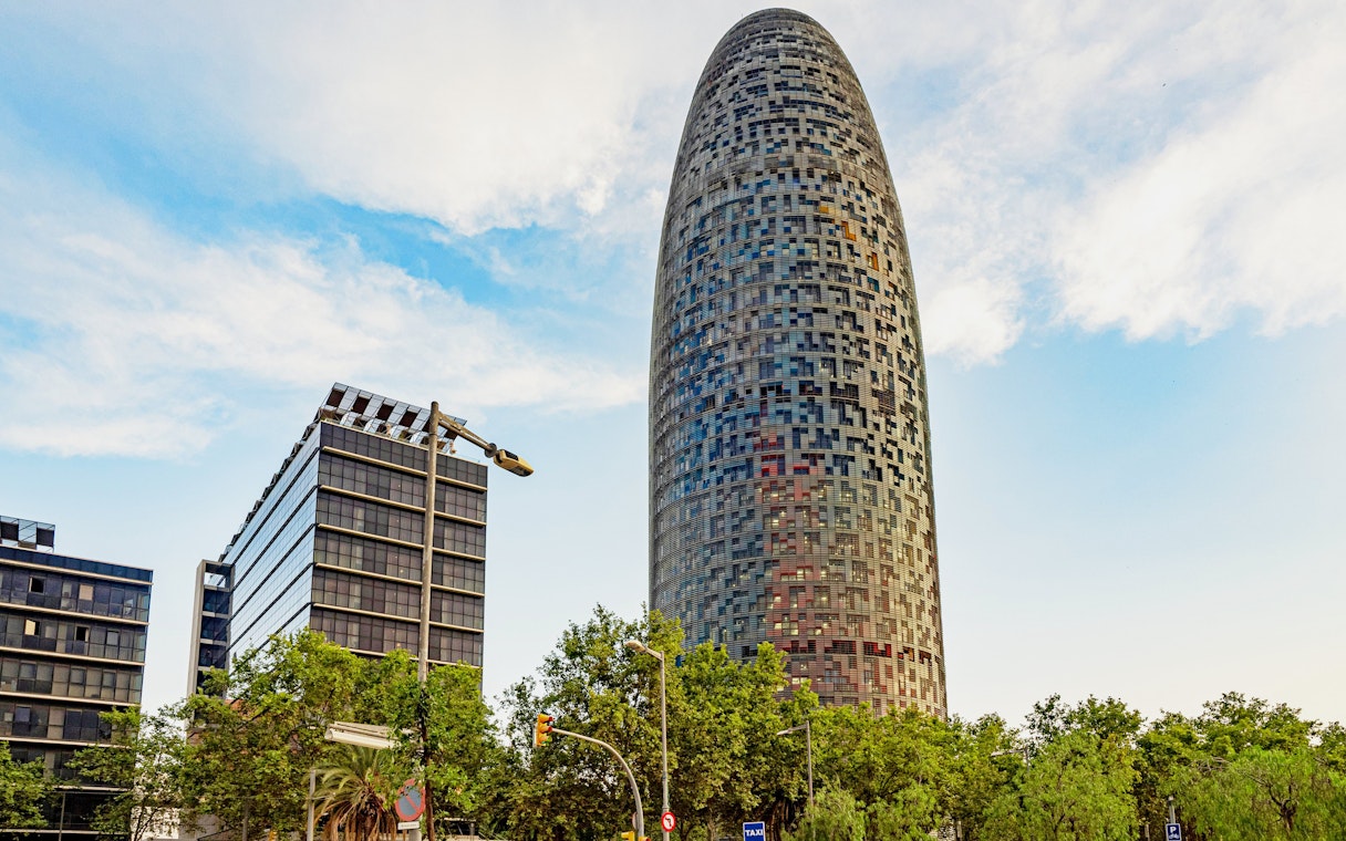 Torre Glòries in Barcelona with surrounding modern buildings and trees.