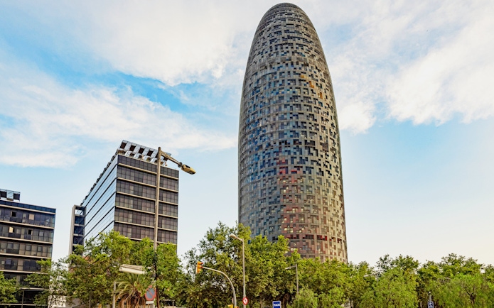 Torre Glòries in Barcelona with surrounding modern buildings and trees.