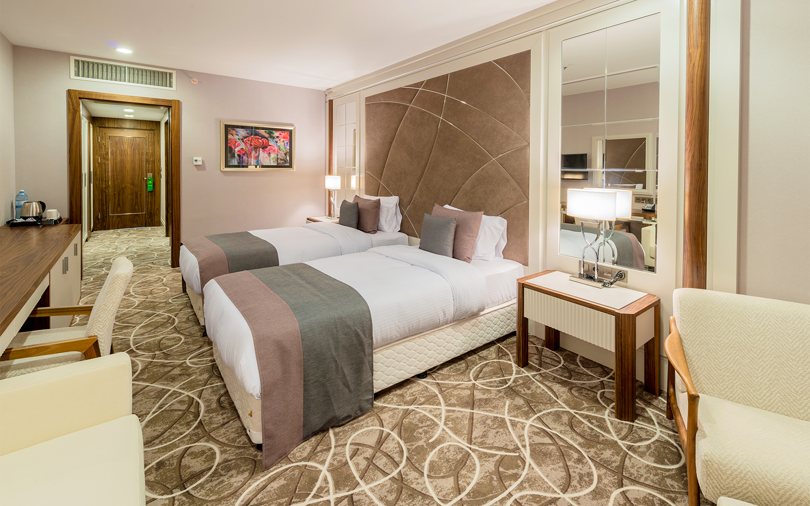 Twin beds in a mid-range hotel room with modern decor and a large mirror.