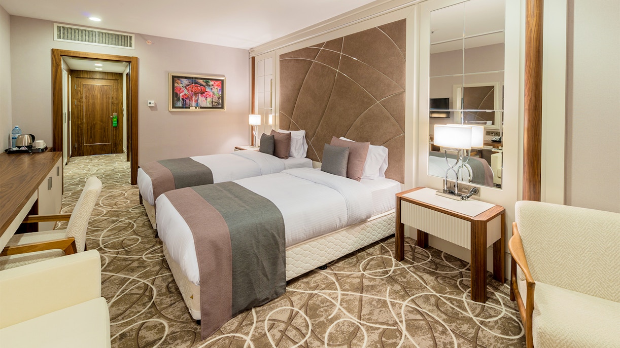 Twin beds in a mid-range hotel room with modern decor and a large mirror.