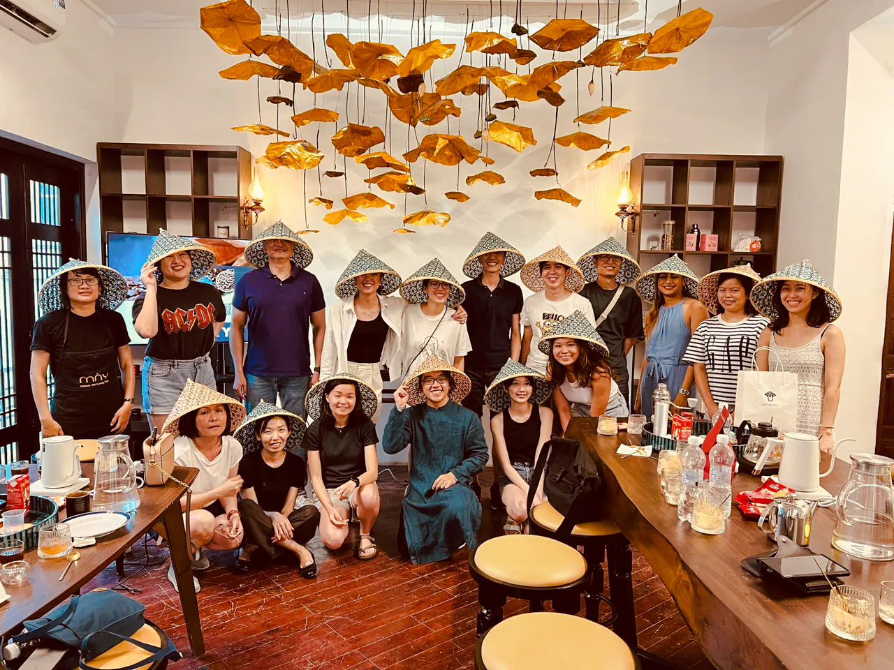 Group enjoying Vietnamese coffee class in Hanoi, wearing traditional hats, surrounded by cultural decor.