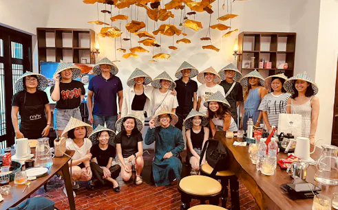 Group enjoying Vietnamese coffee class in Hanoi, wearing traditional hats, surrounded by cultural decor.