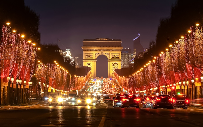 Champs-Élysées illuminated at evening with Arc de Triomphe in the background.