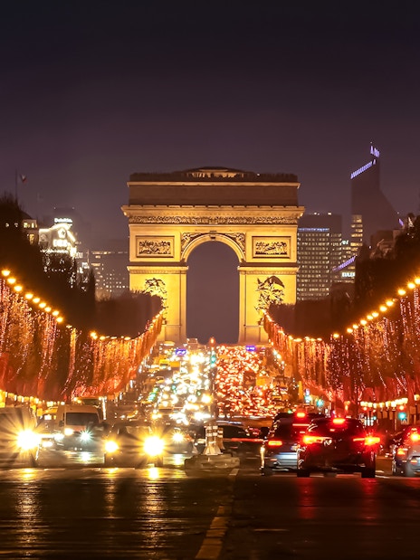 Champs-Élysées illuminated at evening with Arc de Triomphe in the background.