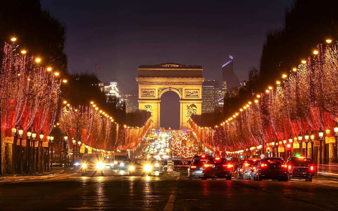 Champs-Élysées illuminated at evening with Arc de Triomphe in the background.