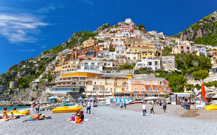 Colorful hillside buildings overlooking Positano beach with people relaxing on the shore.