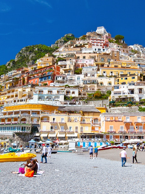 Colorful hillside buildings overlooking Positano beach with people relaxing on the shore.