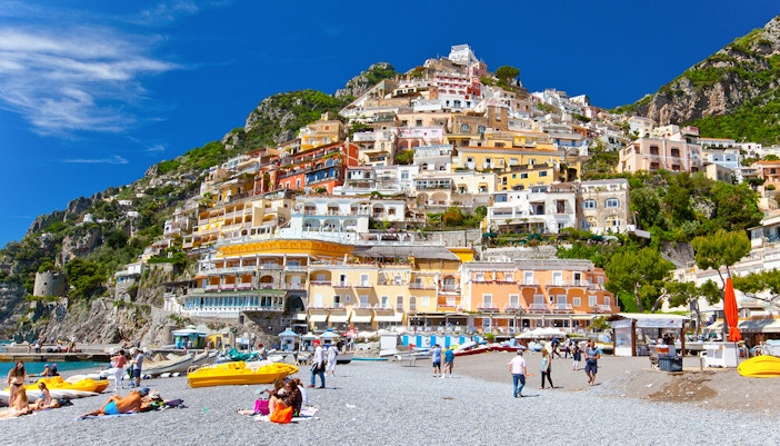 Colorful hillside buildings overlooking Positano beach with people relaxing on the shore.