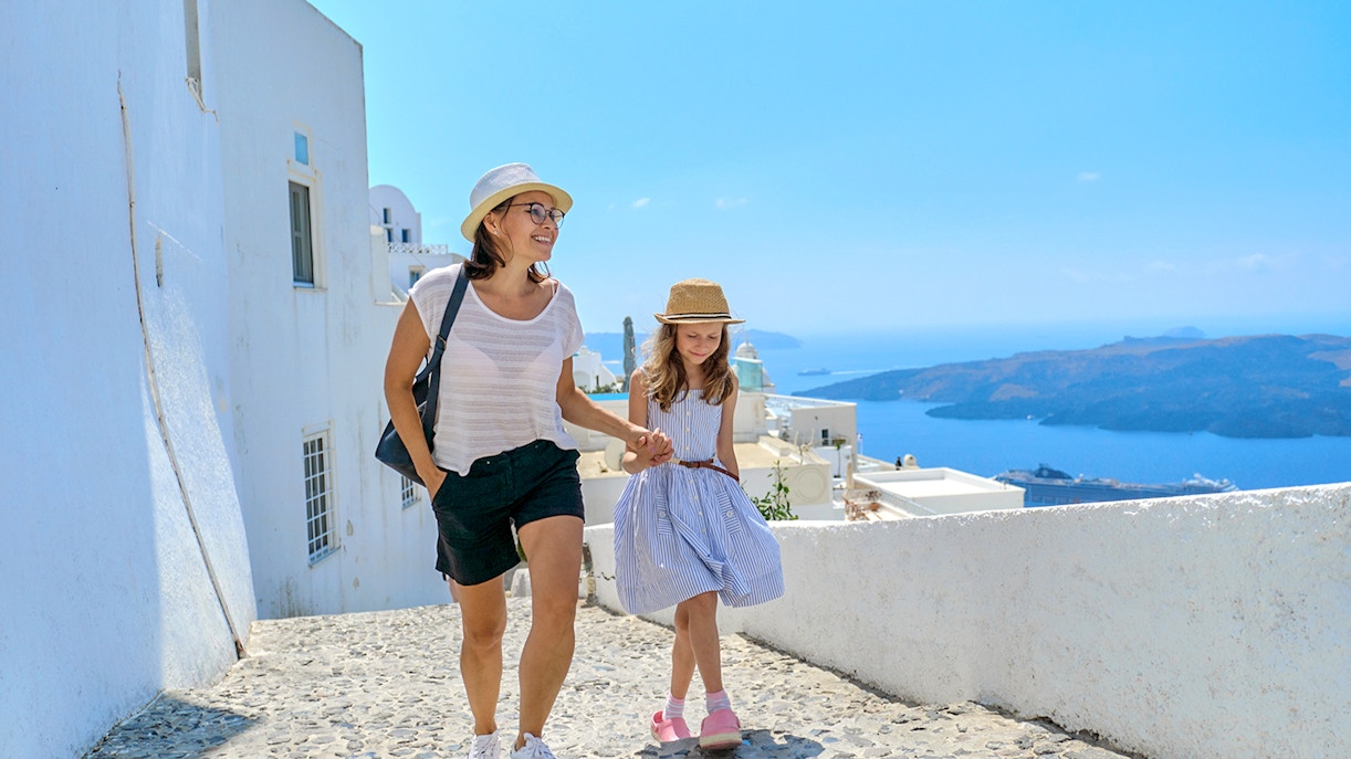 Mother and daughter walking on a cobblestone path in Santorini, Greece, with sea view.