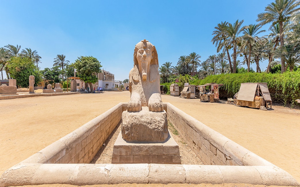 Alabaster sphinx at Memphis, Egypt, surrounded by palm trees and market stalls.