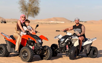 Two people riding quad bikes in the Abu Dhabi desert during a safari tour.