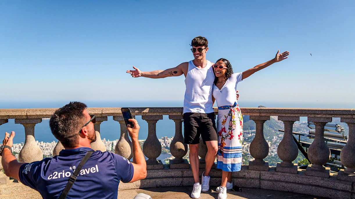 Couple posing at Christ the Redeemer viewpoint, Rio de Janeiro, with cityscape in background.