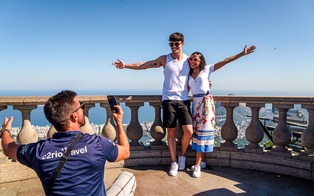 Couple posing at Christ the Redeemer viewpoint, Rio de Janeiro, with cityscape in background.