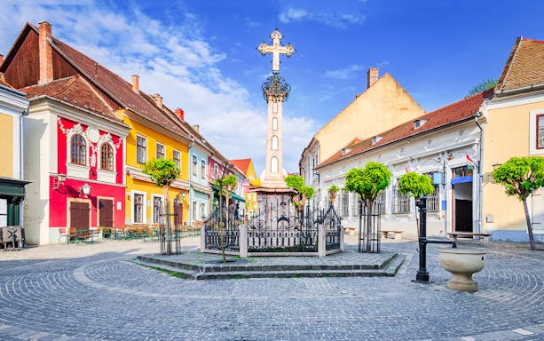 Szentendre village center with colorful buildings and a central cross monument.