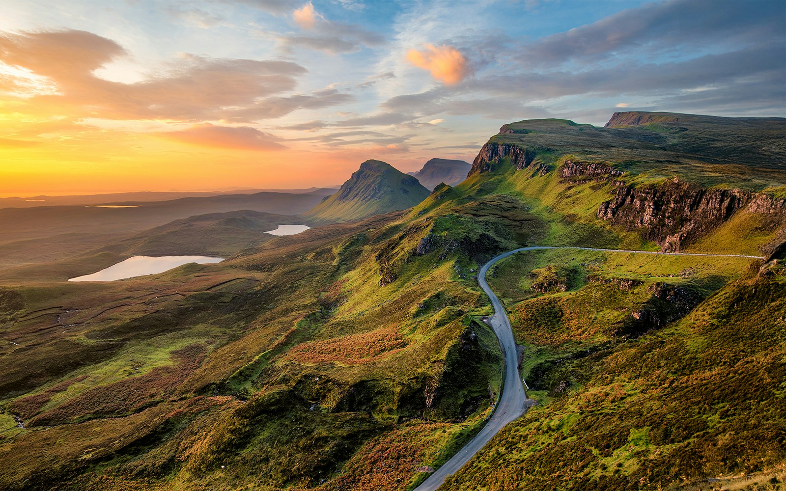 Sunrise over rolling hills and lochs in the Scottish Highlands.