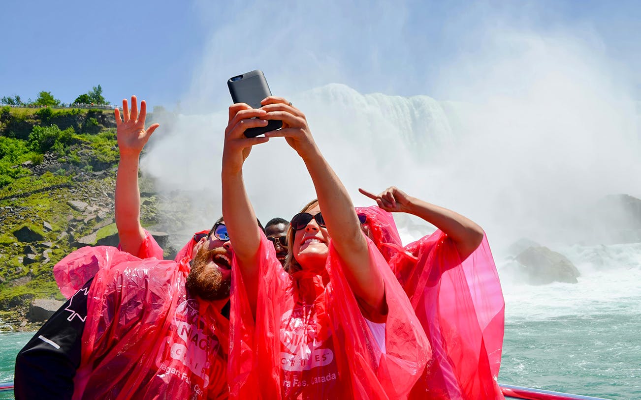 Tourists in red ponchos taking a selfie on a Niagara Falls boat tour.