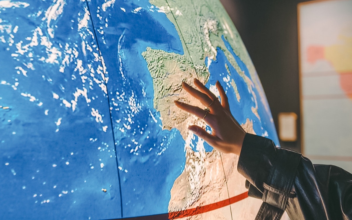 Hand touching a map of Europe, highlighting Spain for The Wine Experience tour.