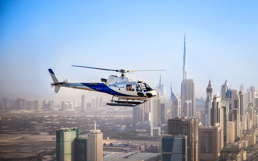 Helicopter flying over Dubai skyline with Burj Khalifa in view.
