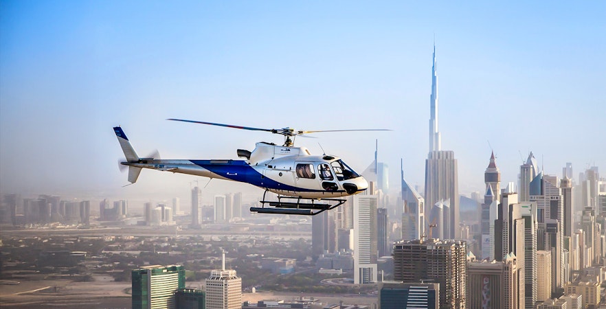 Helicopter flying over Dubai skyline with Burj Khalifa in view.