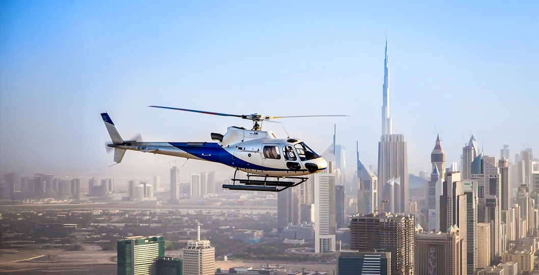 Helicopter flying over Dubai skyline with Burj Khalifa in view.