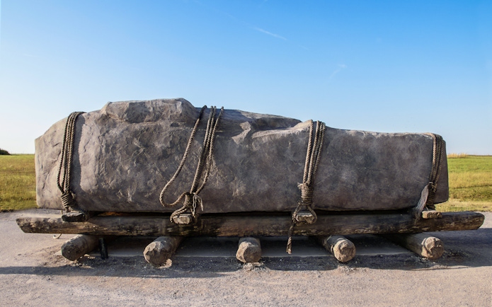 Stone on wooden sledge with rollers and ropes, illustrating ancient transport methods.