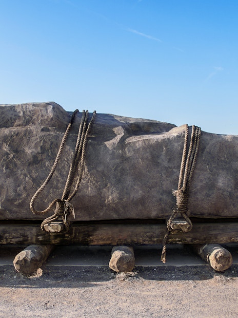 Stone on wooden sledge with rollers and ropes, illustrating ancient transport methods.