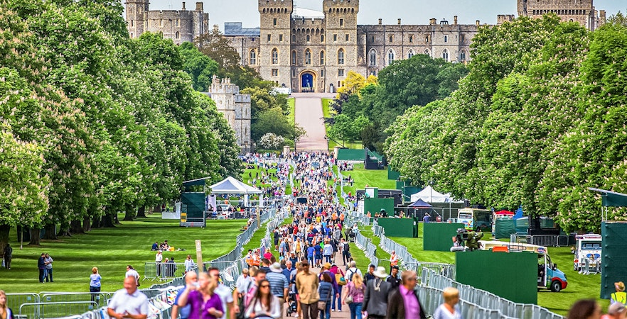 Windsor Castle's stone facade with visitors in lush green surroundings, England.