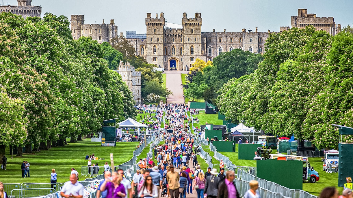 Windsor Castle's stone facade with visitors in lush green surroundings, England.