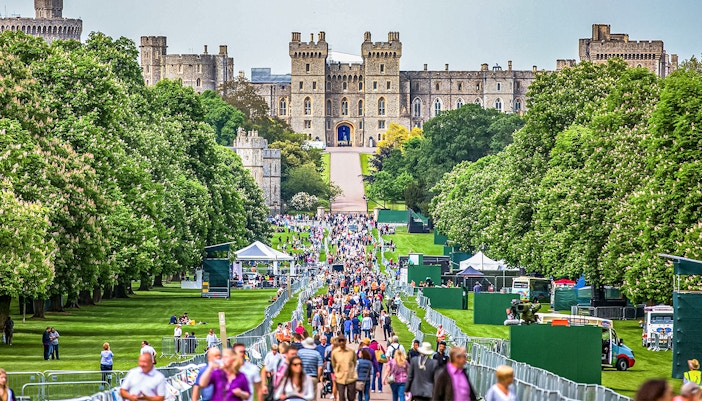 Windsor Castle's stone facade with visitors in lush green surroundings, England.