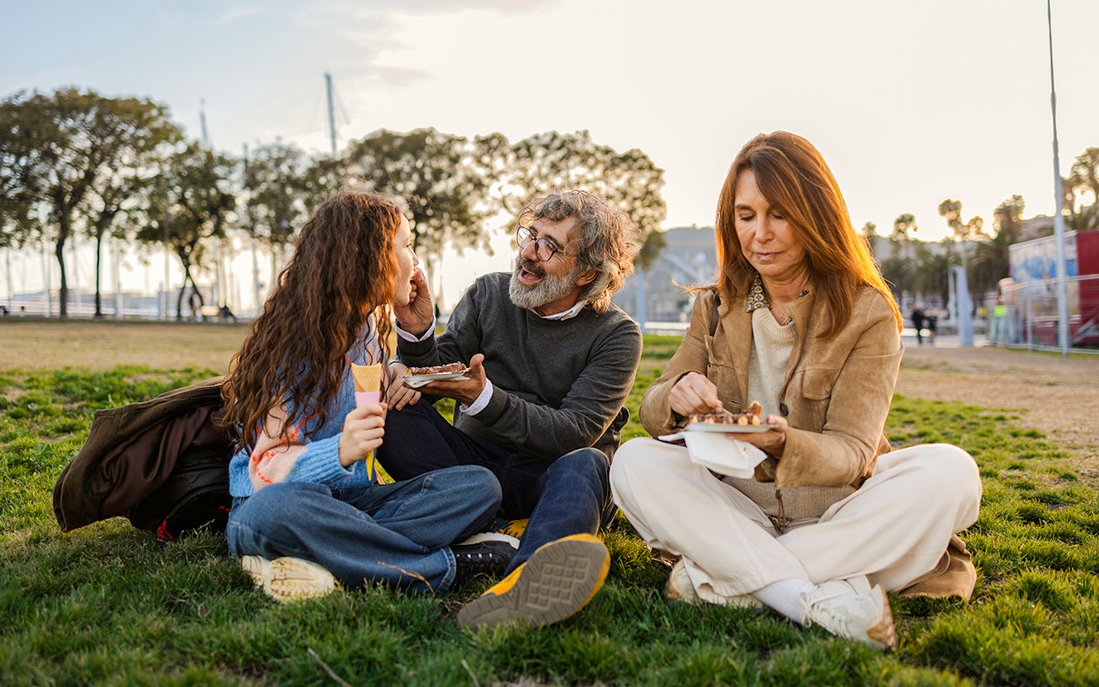 Family having a picnic in a park with trees and a marina in the background.