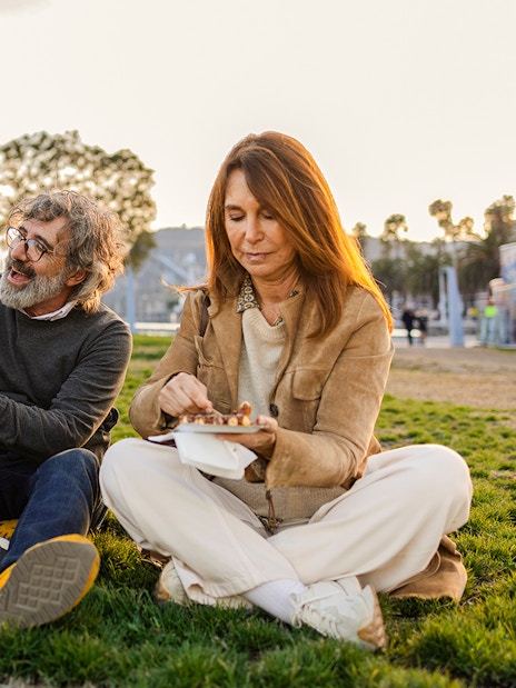 Family having a picnic in a park with trees and a marina in the background.