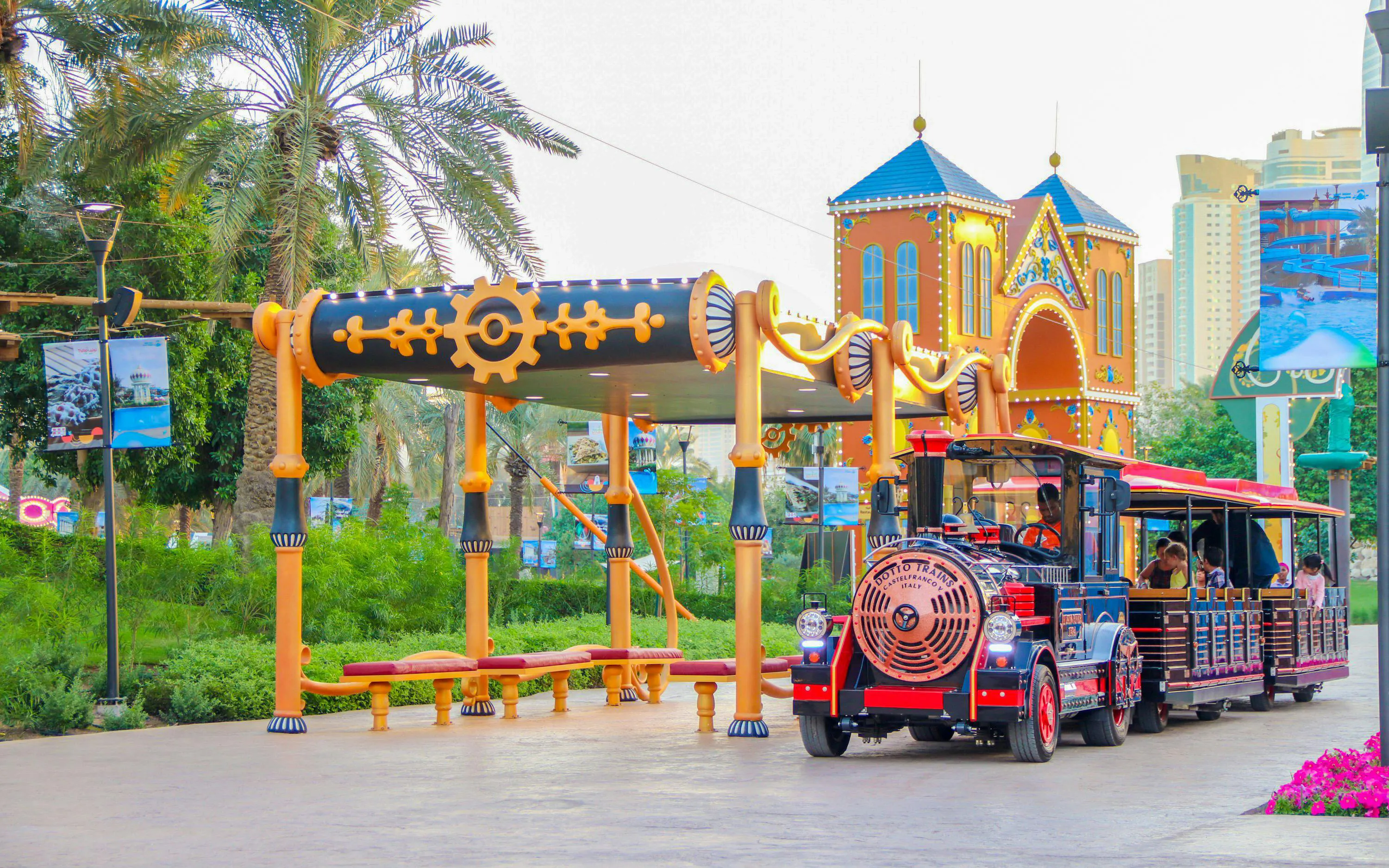Time train ride at Al Montazah Parks, Island of Legends, with colorful station and palm trees.