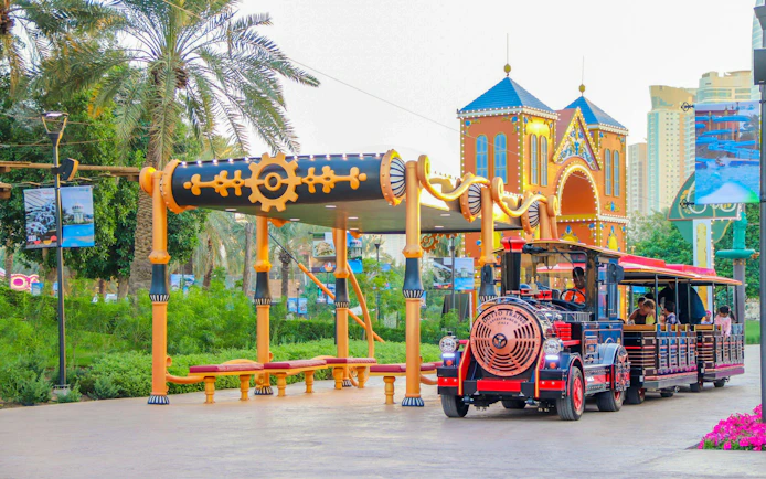 Time train ride at Al Montazah Parks, Island of Legends, with colorful station and palm trees.