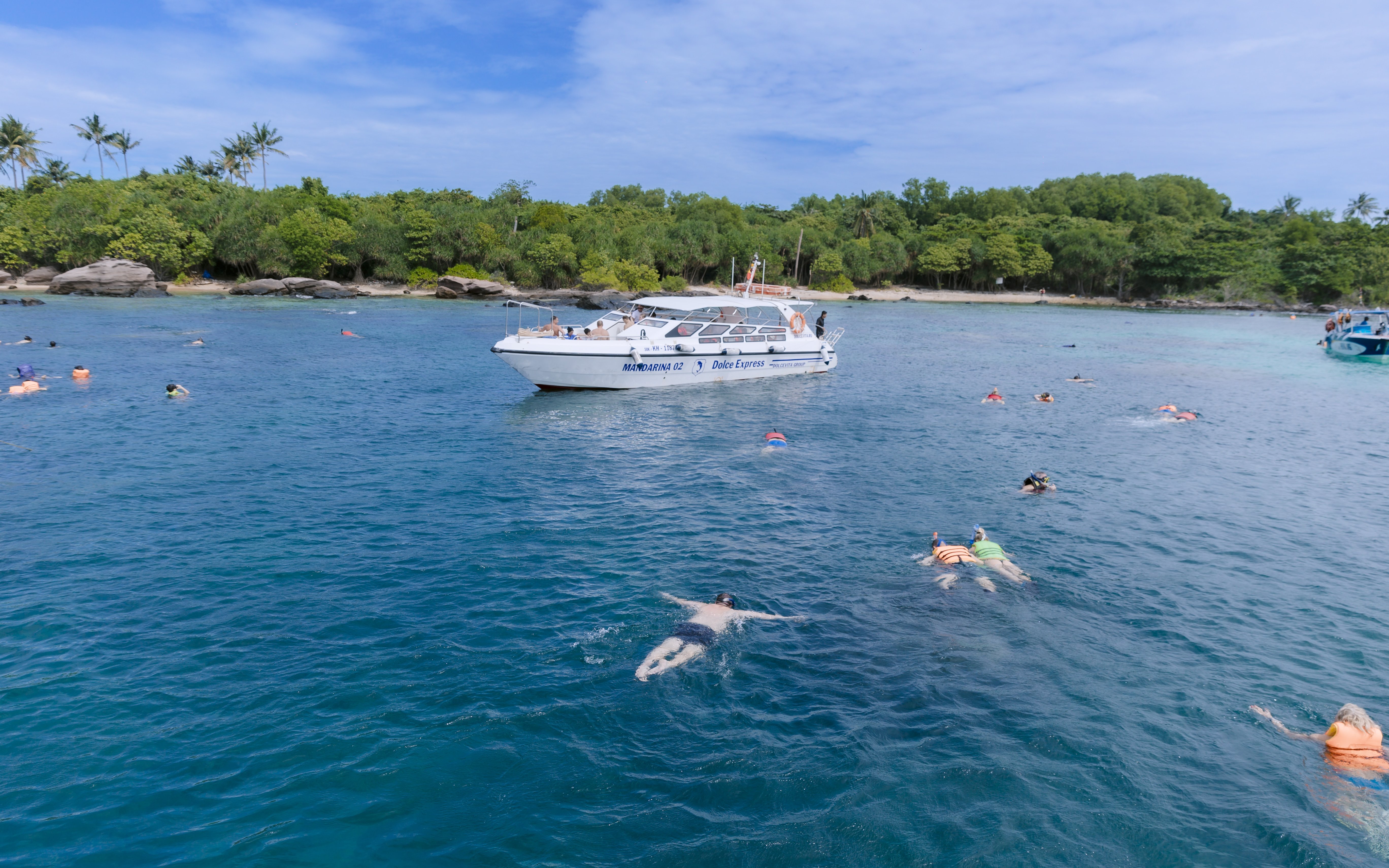 Snorkelers exploring clear waters with speed boat nearby on 4 island day trip.