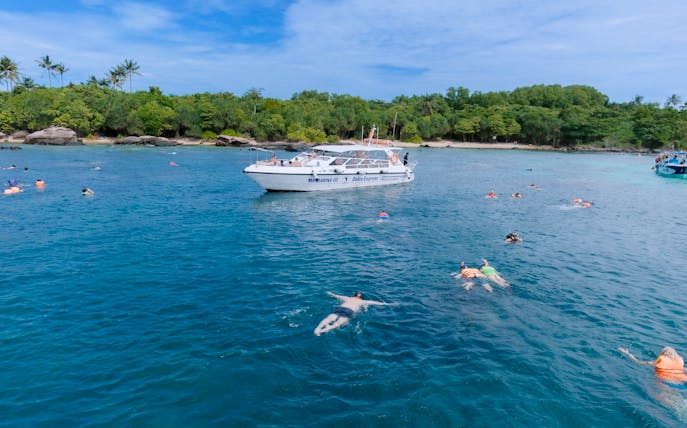 Snorkelers exploring clear waters with speed boat nearby on 4 island day trip.