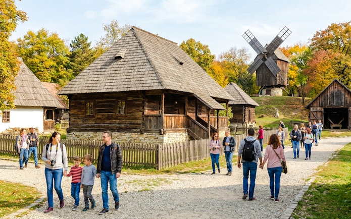 Visitors walking through traditional wooden houses at Village Museum, Bucharest.