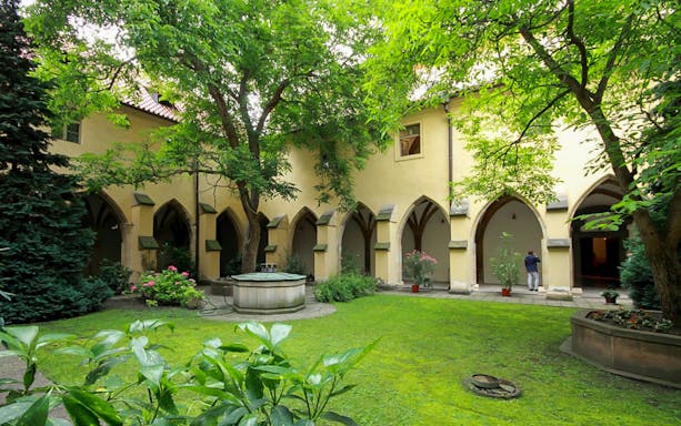 Courtyard of Minorite Monastery of St James in Prague with arches and greenery.