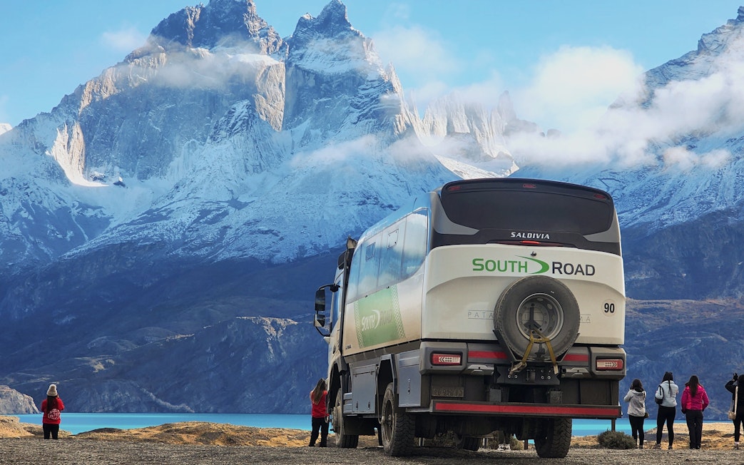 Tourist vehicle with visitors in Torres del Paine National Park, Chile, with mountains in the background.