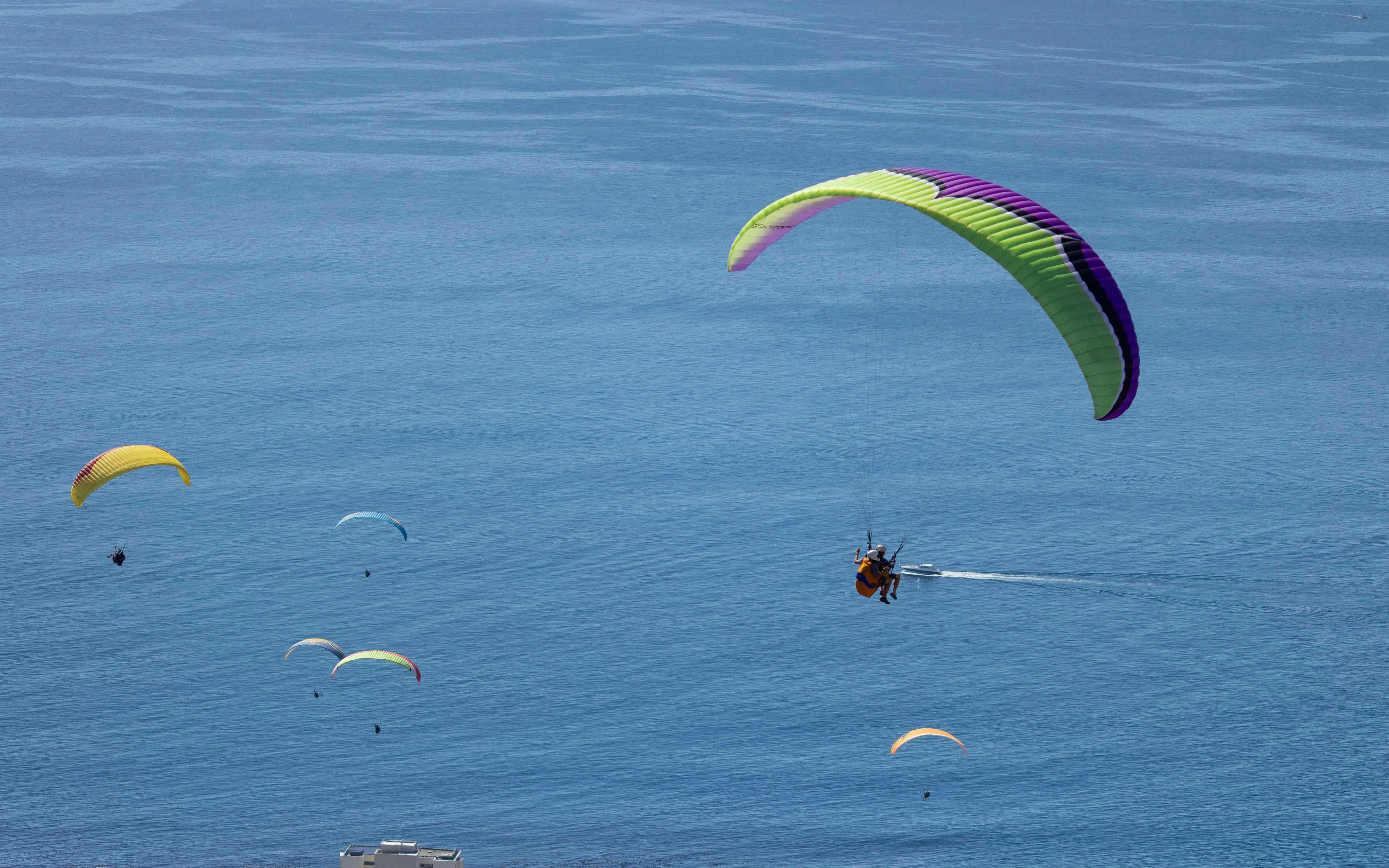 Tandem paragliders soaring over ocean near Cape Town.