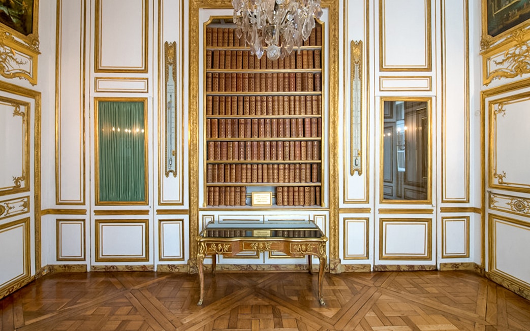 Bookshelf and ornate table in the Palace of Versailles library room.